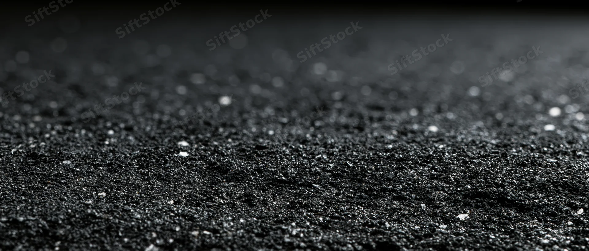 Close-up of dark asphalt surface with scattered gravel and shallow depth of field