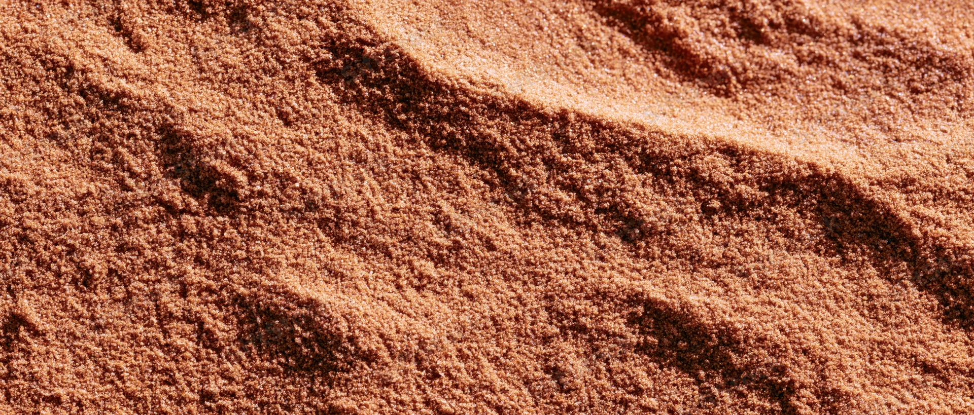 Close-up of coarse dry sand surface with ripples and texture filling the frame