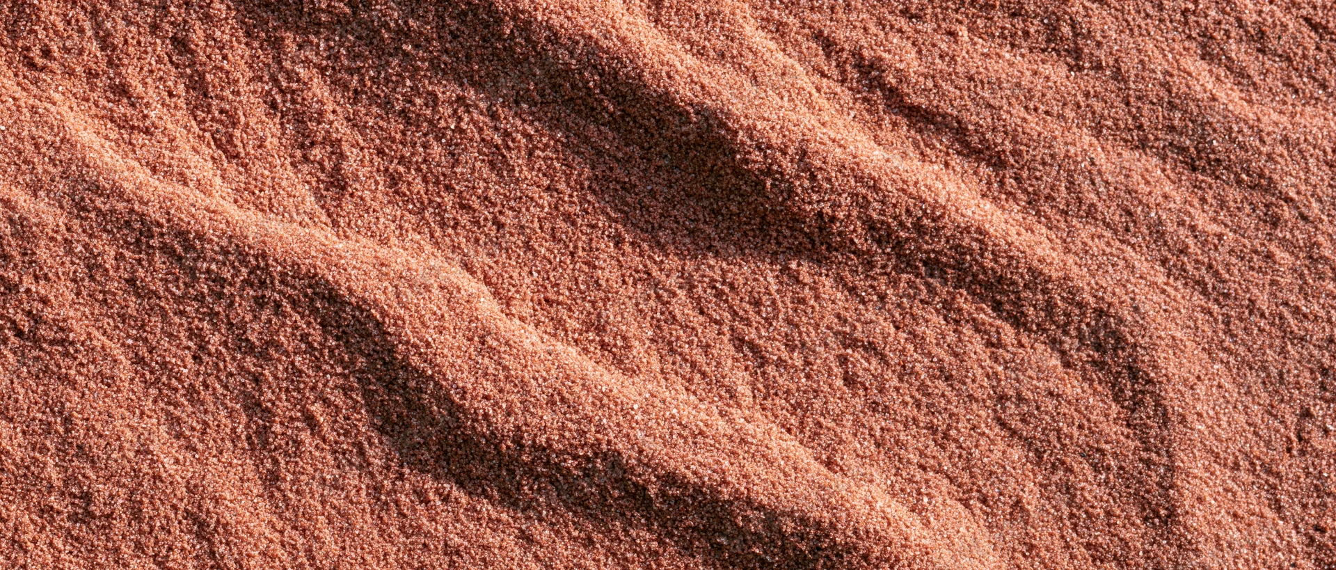 Closeup of coarse dry sand surface with rippled texture filling the frame