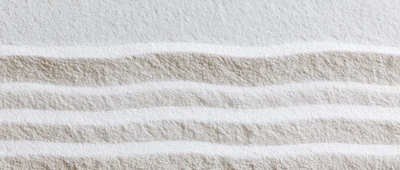 Raked white sand in a zen garden forming horizontal stripes with soft texture