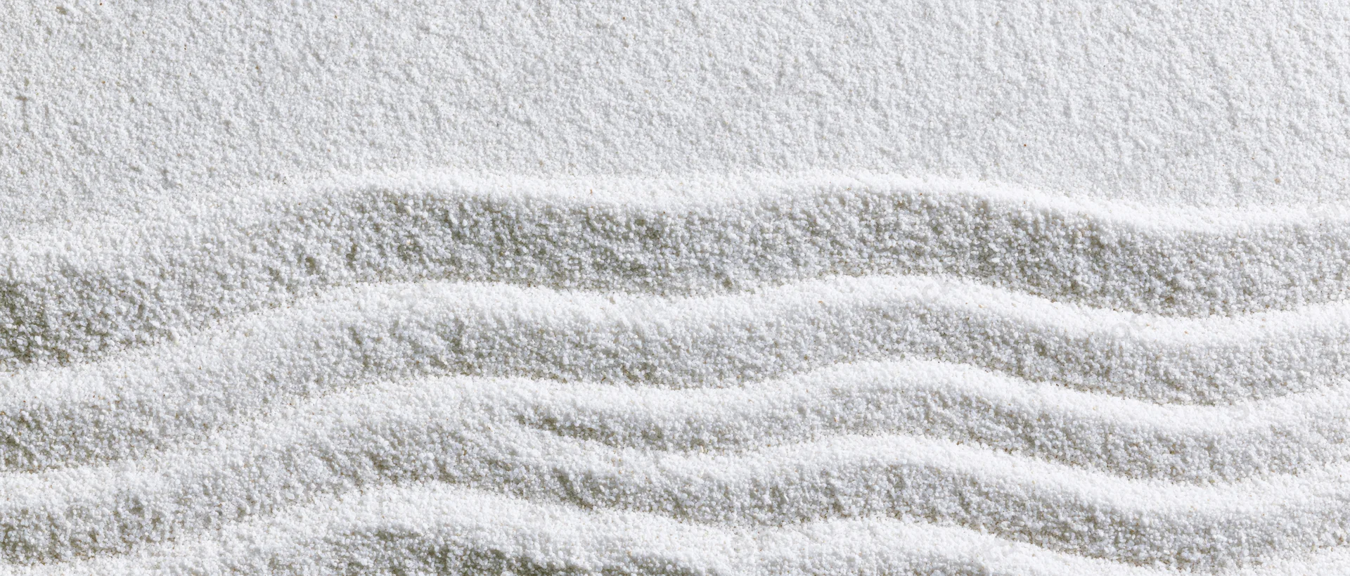 Raked white sand in a zen garden forming wavy lines across the surface