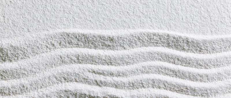 Raked white sand in a zen garden forming wavy lines across the surface