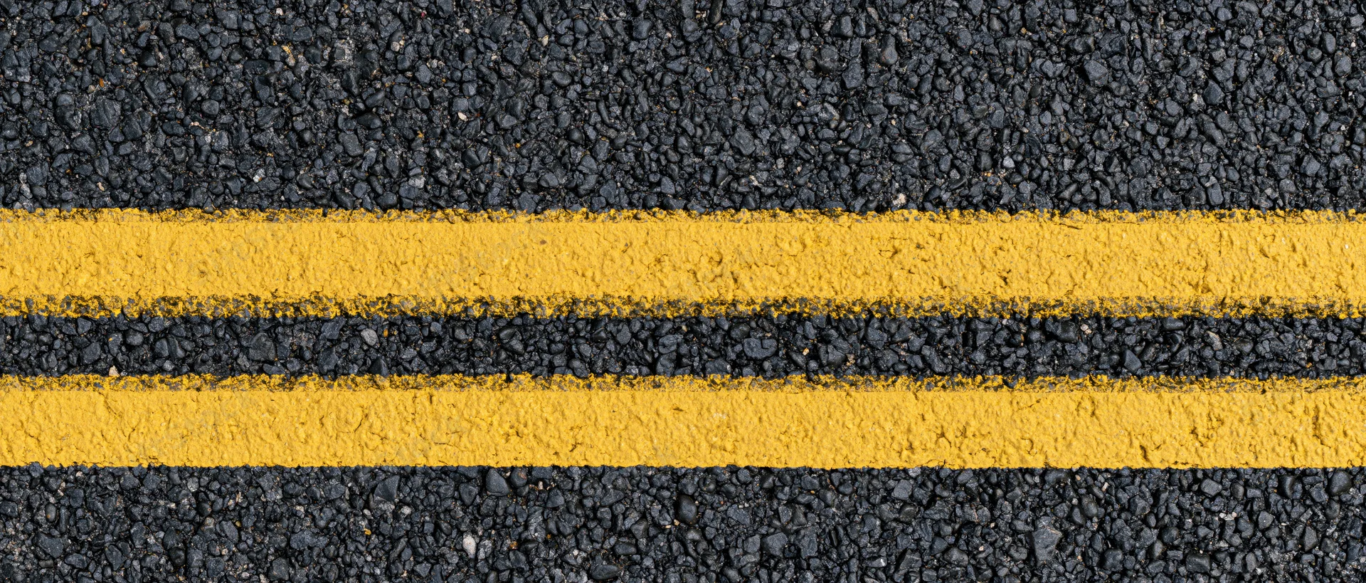 Close-up overhead view of double yellow lines on fresh asphalt road surface