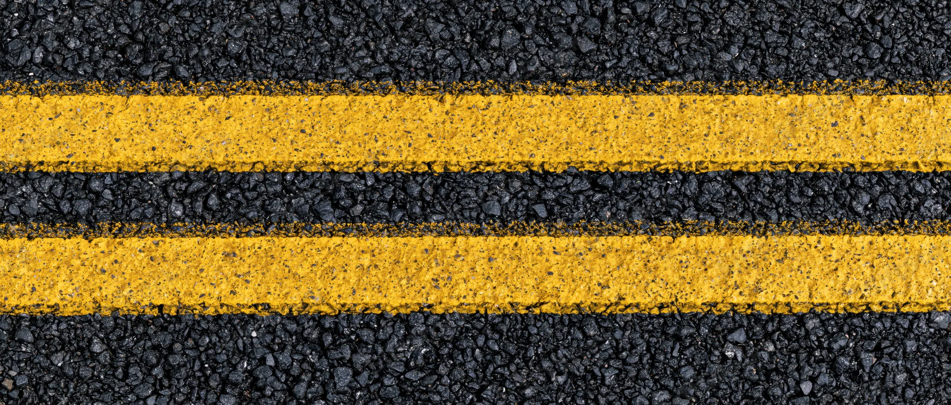 Close-up overhead view of double yellow lines on fresh asphalt road surface