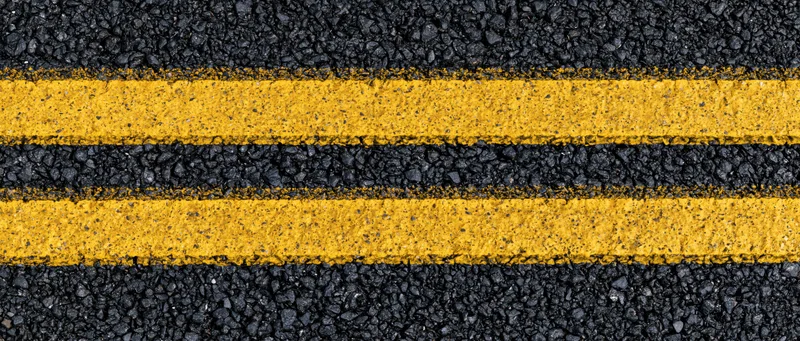 Close-up overhead view of double yellow lines on fresh asphalt road surface