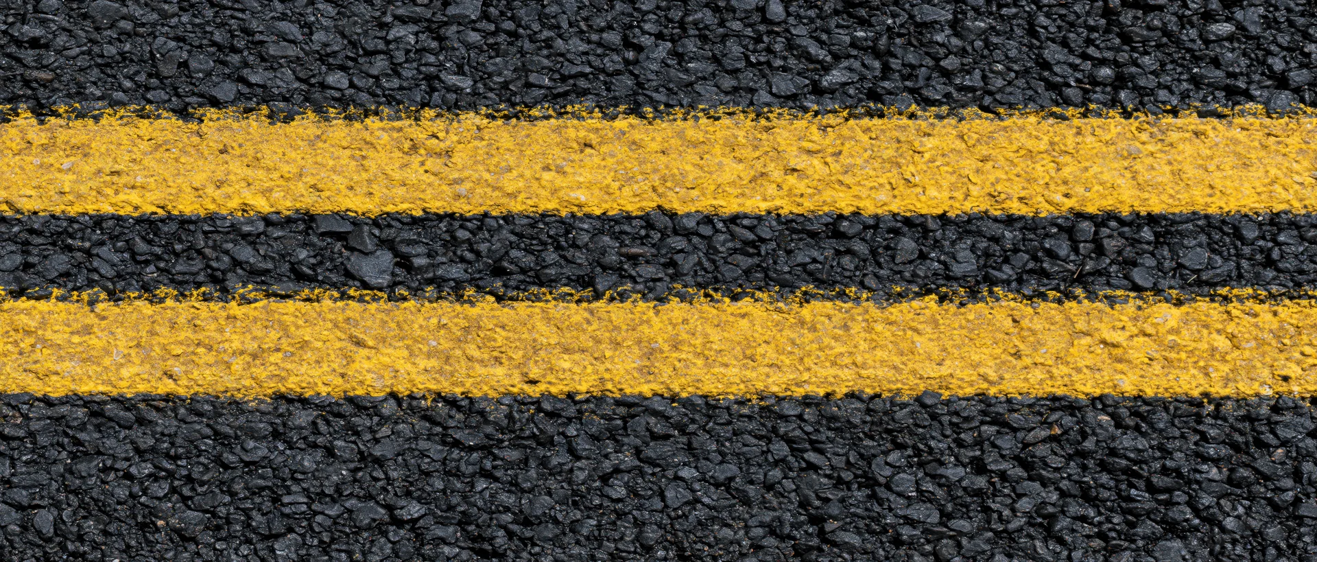 Close-up overhead view of double yellow lines on fresh asphalt road surface