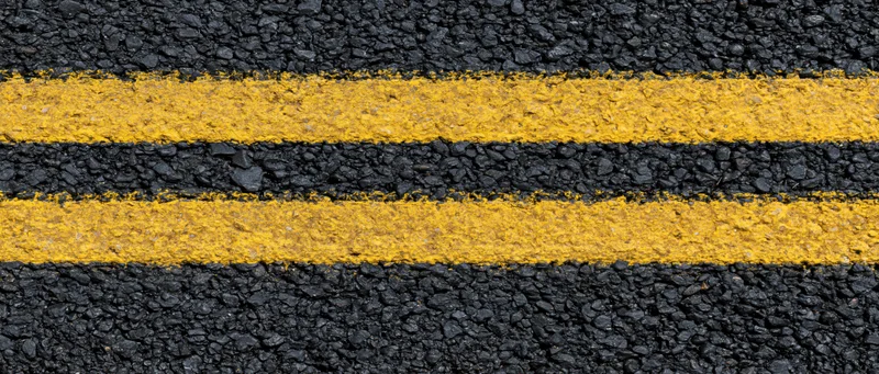 Close-up overhead view of double yellow lines on fresh asphalt road surface