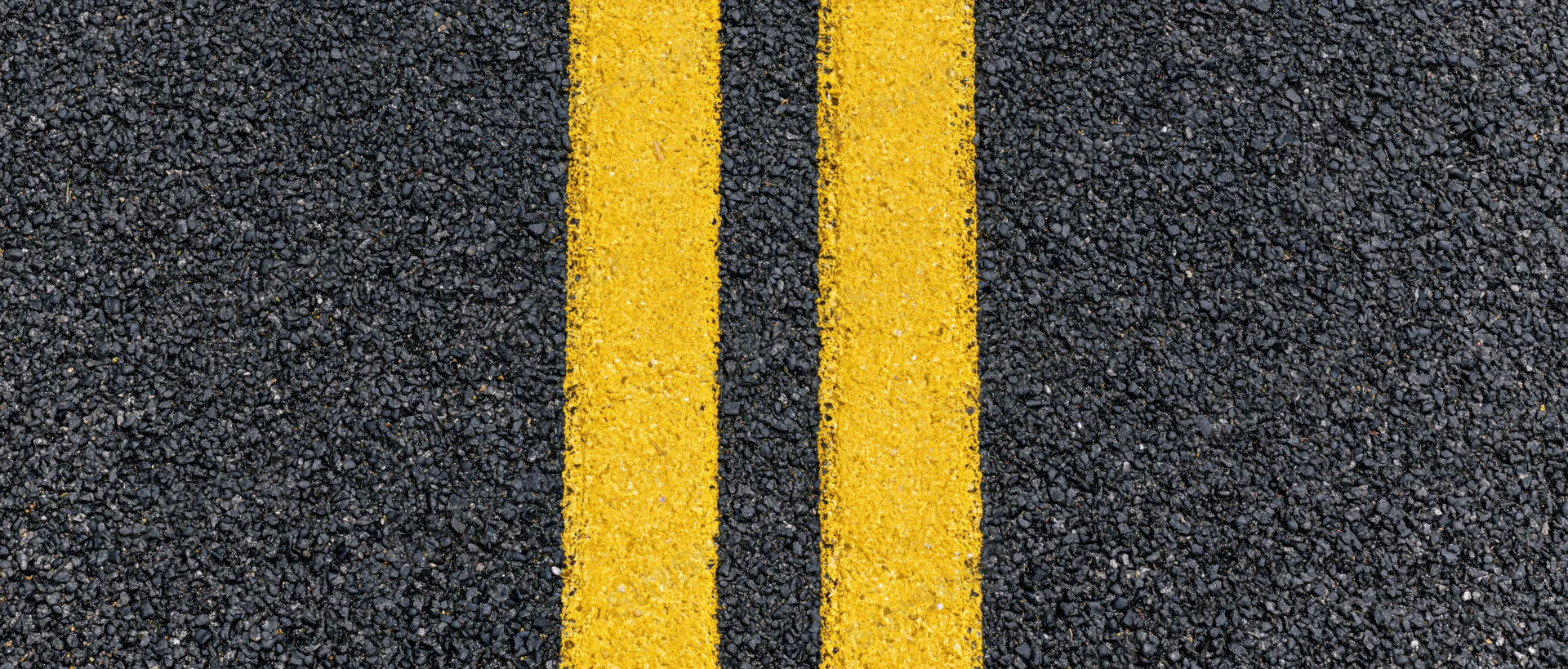 Close-up overhead view of double yellow lines on fresh asphalt road surface