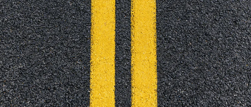 Close-up overhead view of double yellow lines on fresh asphalt road surface