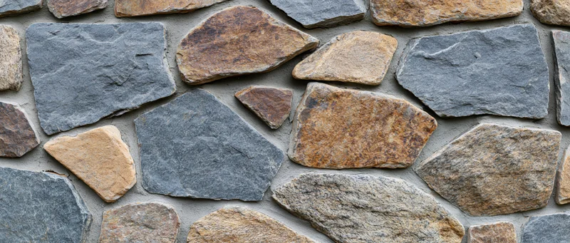 Close-up of a dry-stack rubble stone wall with irregular gray and brown stones set in mortarless construction