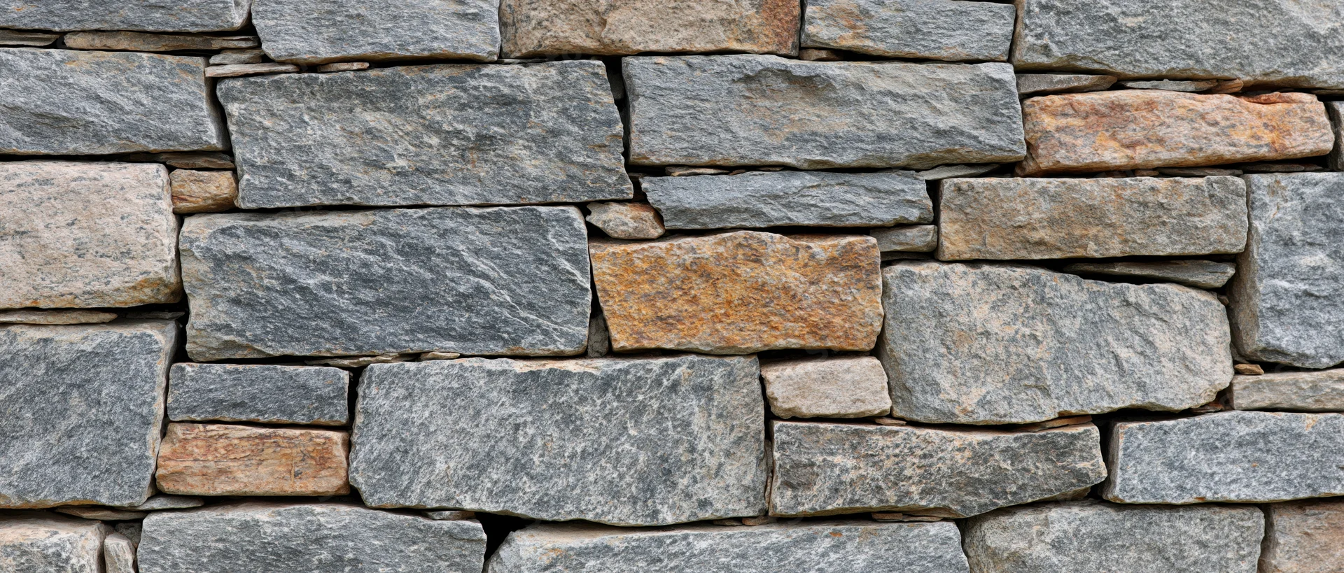 Close-up of a dry-stacked stone wall made of irregular gray and brown rocks arranged in horizontal layers