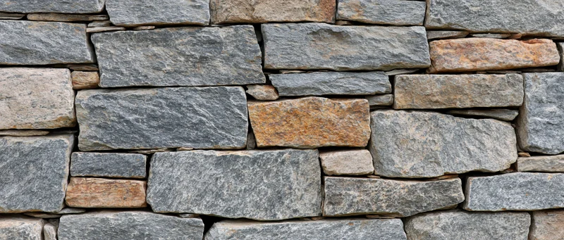 Close-up of a dry-stacked stone wall made of irregular gray and brown rocks arranged in horizontal layers