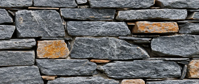 Close-up of a dry-stacked stone wall made of irregular gray and orange rocks arranged in horizontal layers outdoors