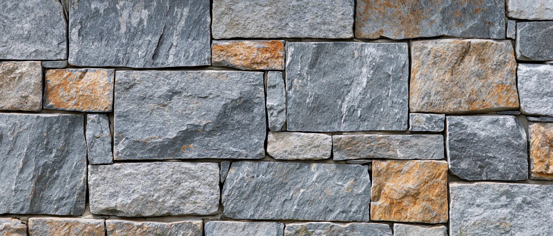 Close-up of a dry-stacked stone wall made of irregular gray and brown stones arranged in a rough pattern on an outdoor facade