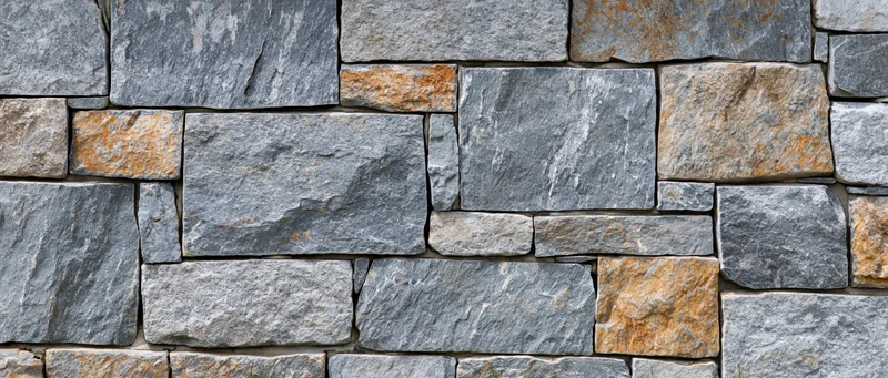 Close-up of a dry-stacked stone wall made of irregular gray and brown stones arranged in a rough pattern on an outdoor facade