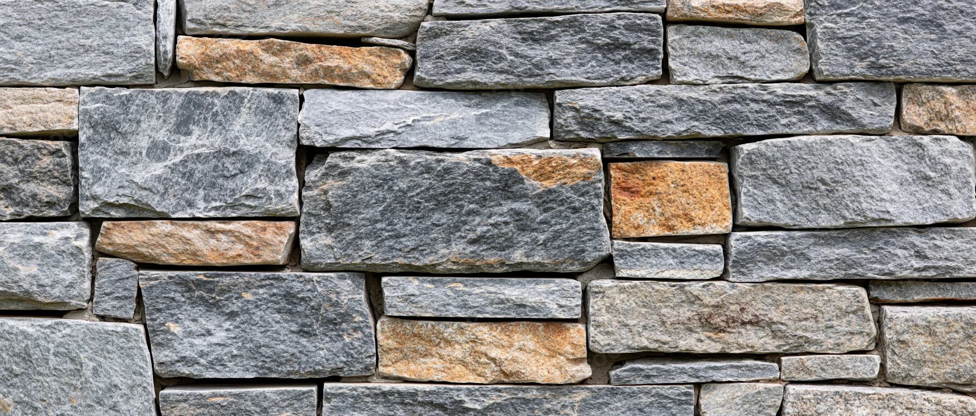 Close-up of a dry-stacked stone wall made of irregular gray and beige stones arranged in horizontal layers