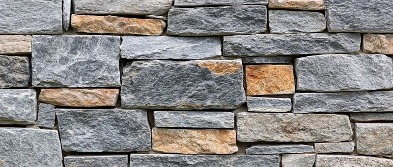 Close-up of a dry-stacked stone wall made of irregular gray and beige stones arranged in horizontal layers
