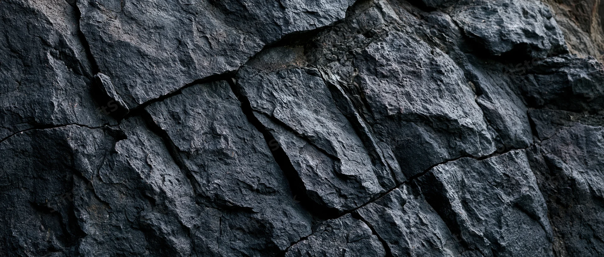 Close-up of a rough dark basalt rock face with visible cracks and layers