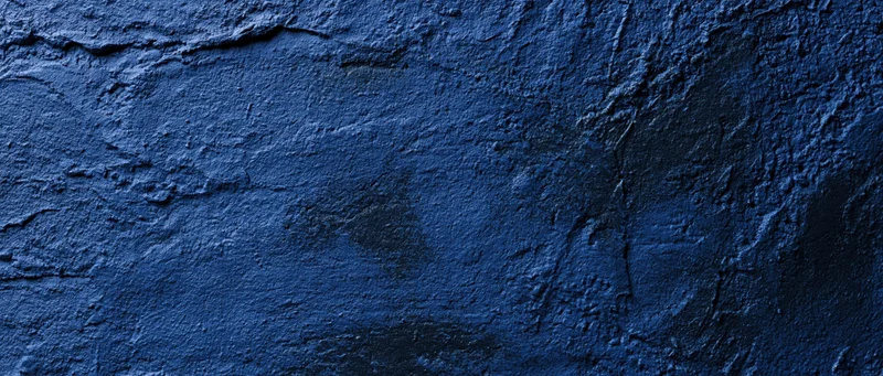 Close-up of a rough blue-painted concrete wall with visible cracks and texture