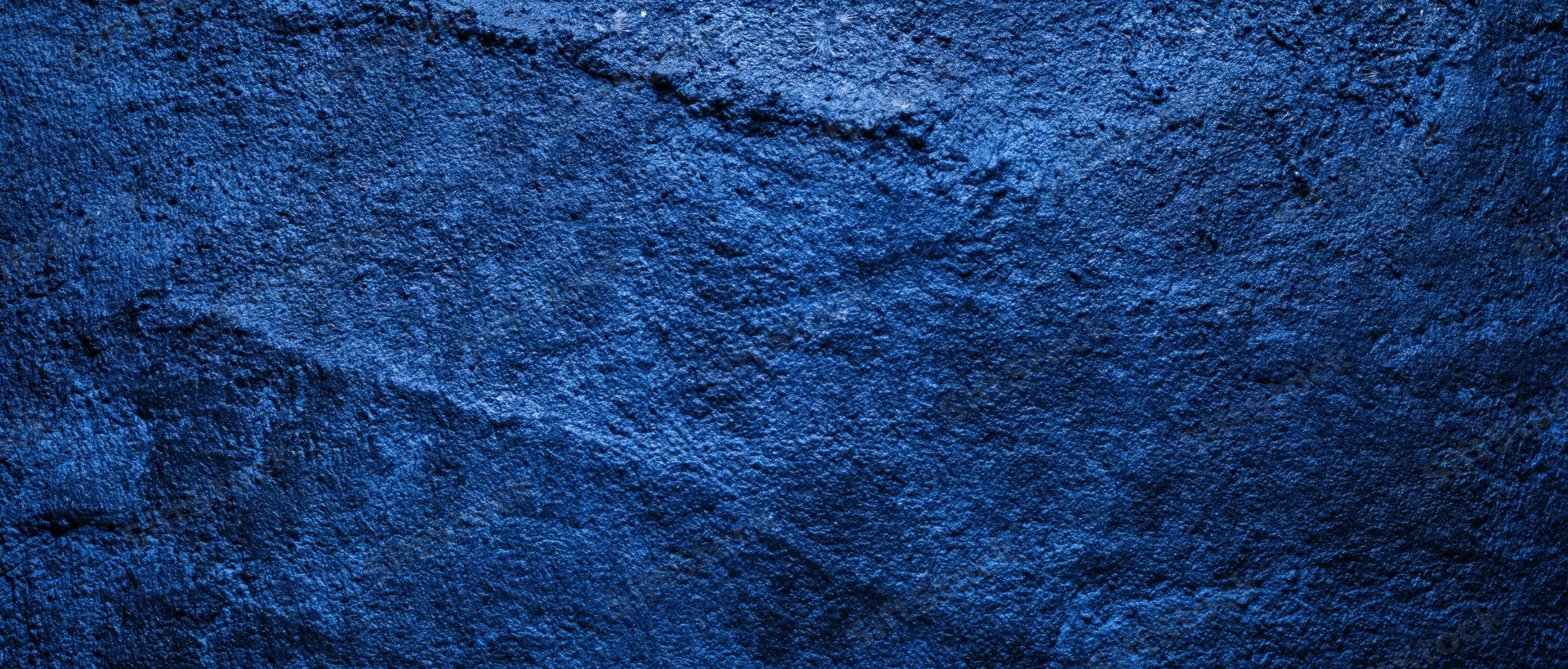 Close-up of a rough blue-painted concrete wall with visible texture and cracks