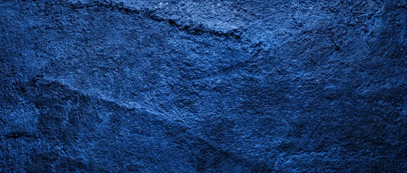 Close-up of a rough blue-painted concrete wall with visible texture and cracks