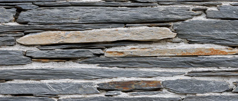 Close-up of stacked slate stone wall with horizontal layers and mortar joints
