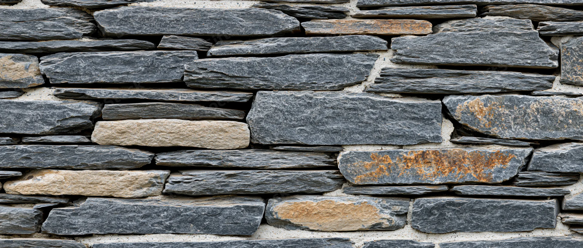 Stacked slate stone wall covering an exterior building facade with gray and beige stones in a rustic pattern