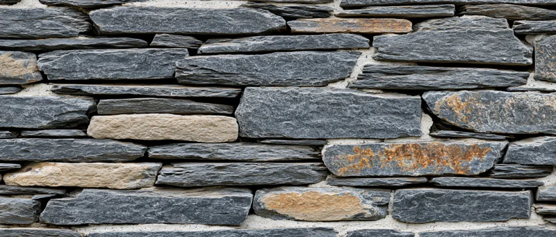 Stacked slate stone wall covering an exterior building facade with gray and beige stones in a rustic pattern