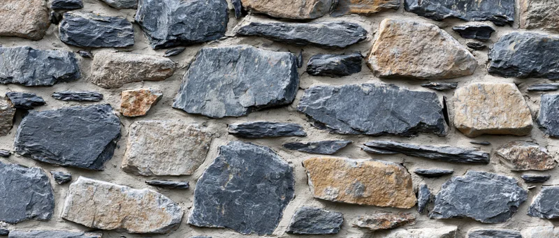 Close-up of an old dry-stone rubble wall with irregularly shaped stones and mortar joints