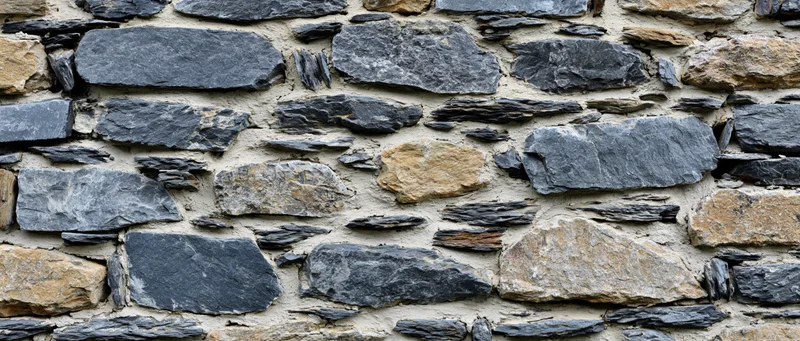 Close-up of an old dry-stone rubble wall with irregularly shaped stones and mortar joints