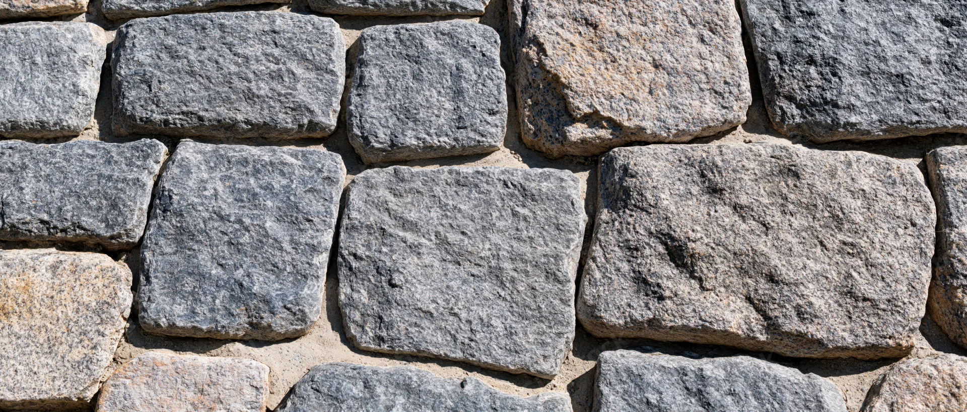 Close-up of an old granite cobblestone wall with rough texture and mortar joints