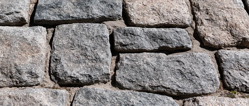 Close-up of old granite cobblestone wall with rough texture and mortar joints
