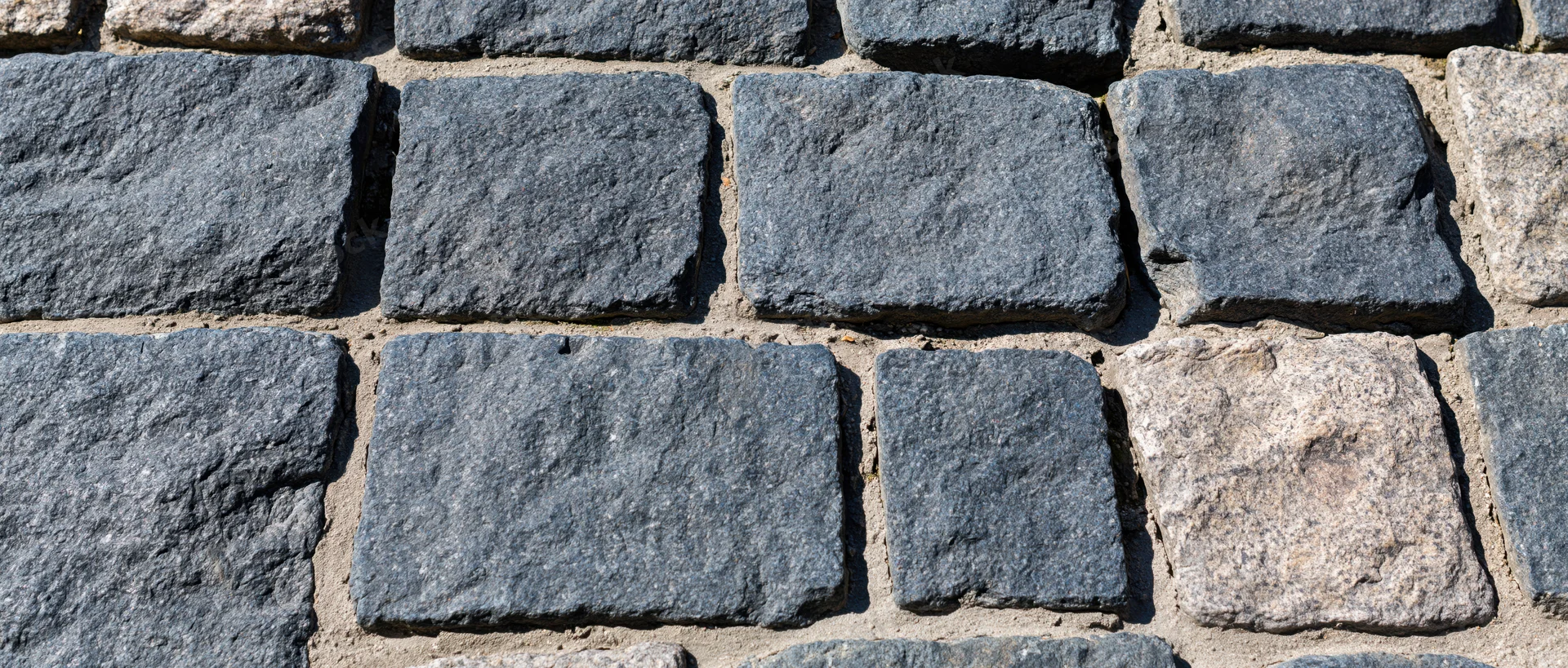 Close-up of old granite cobblestone pavement wall with rough texture and mortar joints
