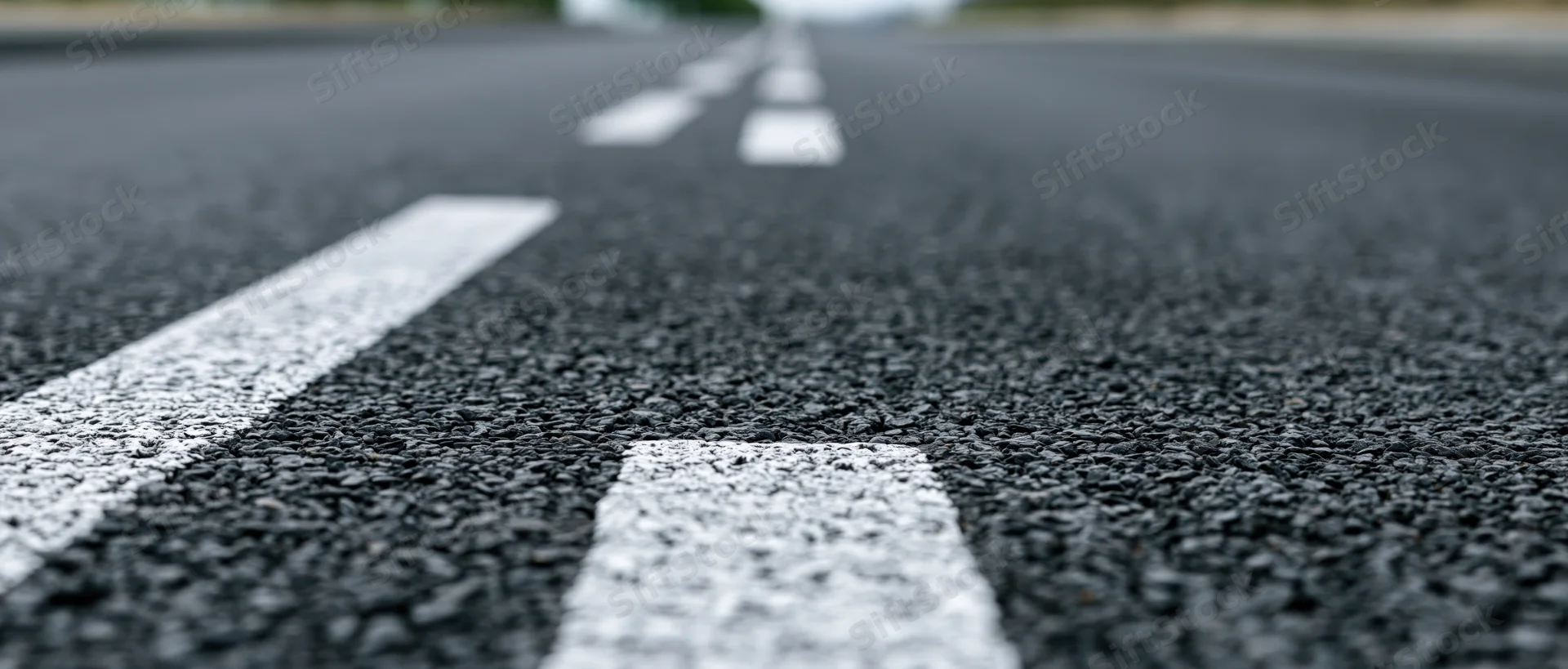 Close-up ground-level view of asphalt road surface with white lane markings receding into the distance