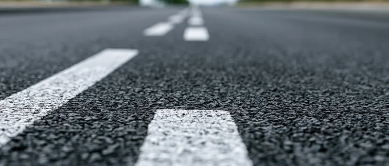 Close-up ground-level view of asphalt road surface with white lane markings receding into the distance