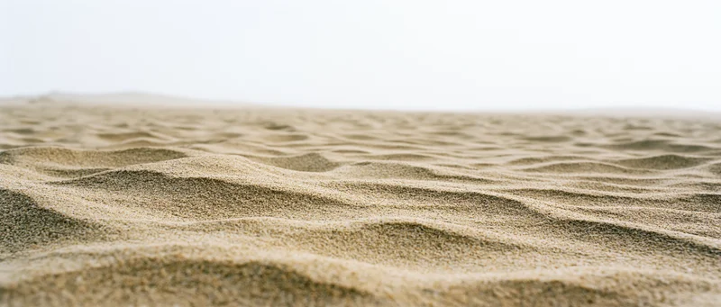 Close-up of rippled dry beach sand with soft waves under bright light
