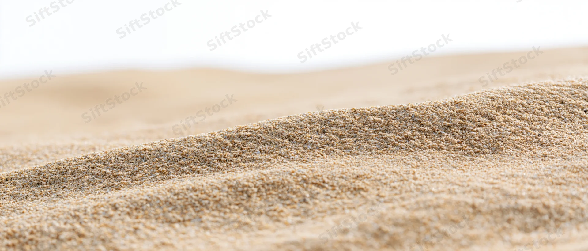 Close-up of undulating dry beach sand texture with wind-formed ripples against a bright background