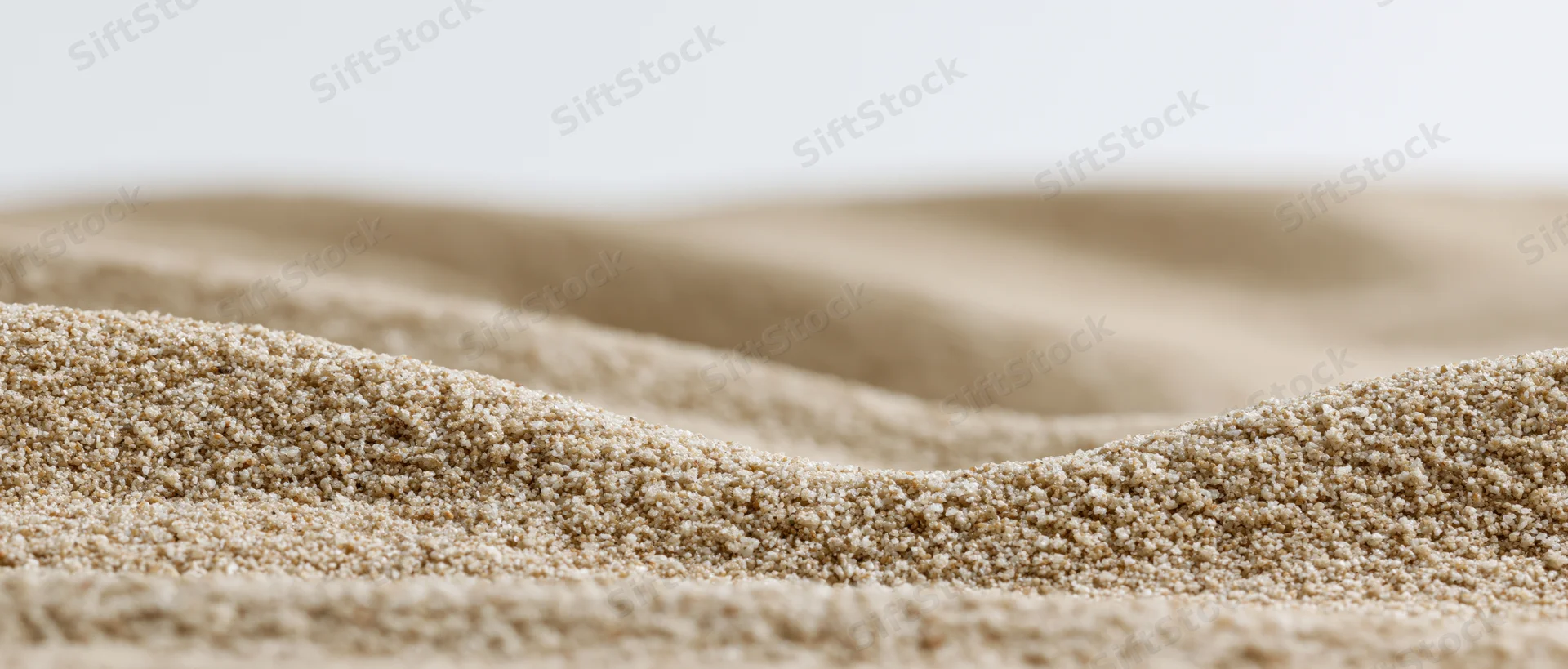 Close-up low-angle view of dry sand ripples forming undulating texture across a smooth surface