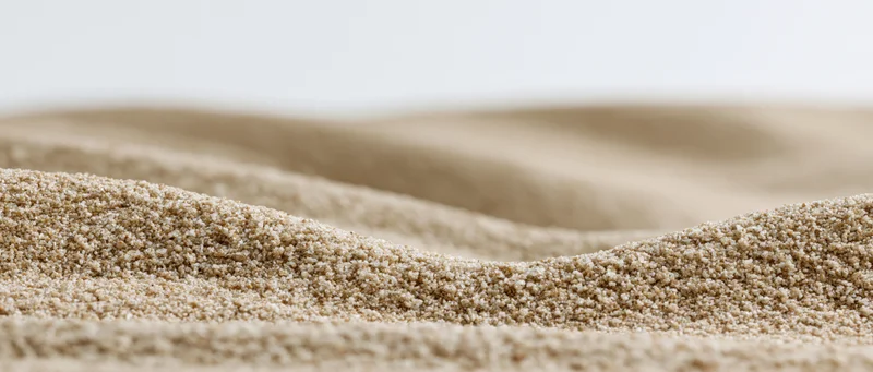 Close-up low-angle view of dry sand ripples forming undulating texture across a smooth surface