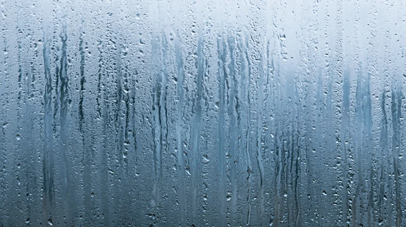 Raindrops streaking down a glass window surface in close-up view