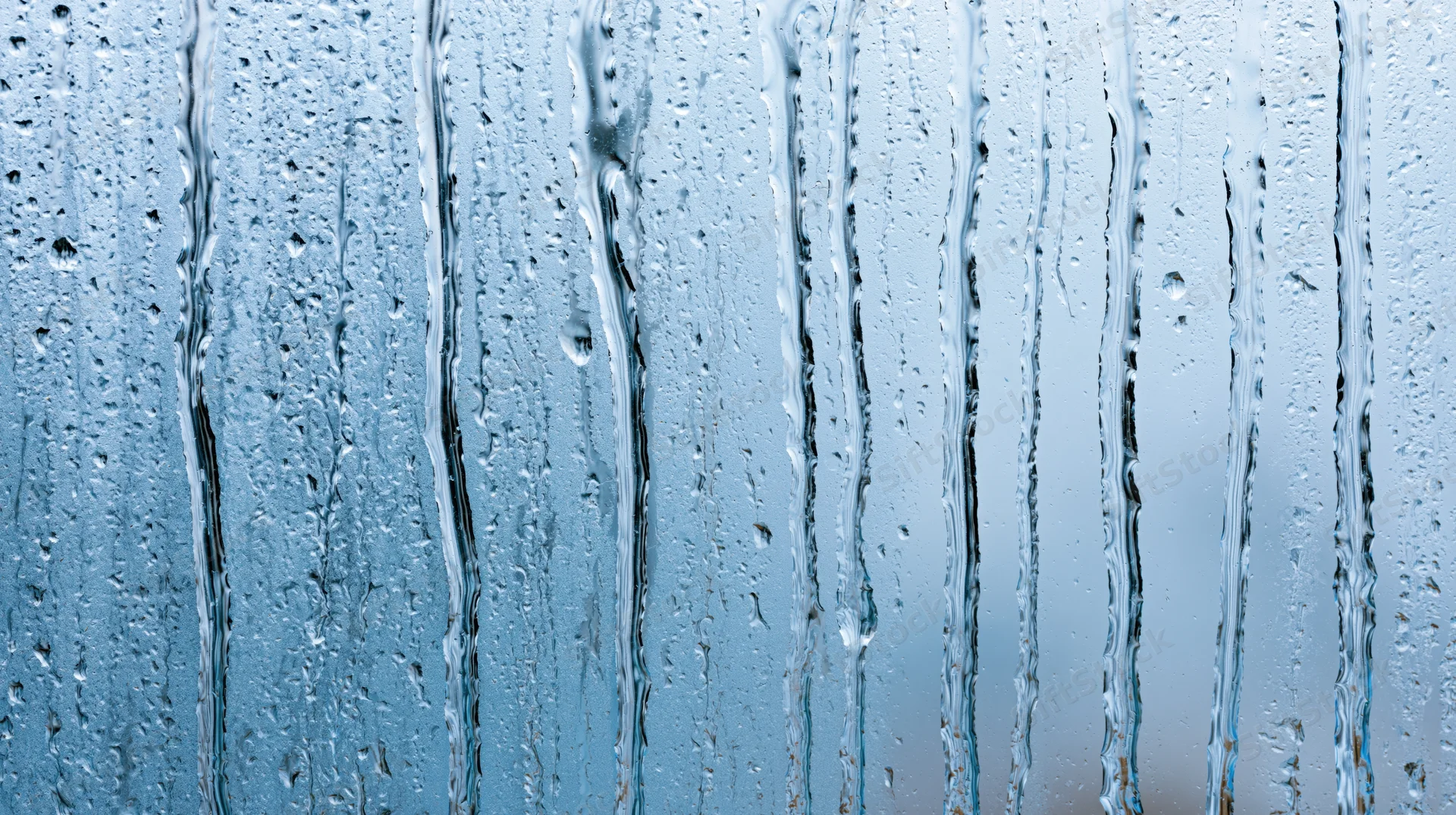 Raindrops streaking down a glass window surface in close-up view