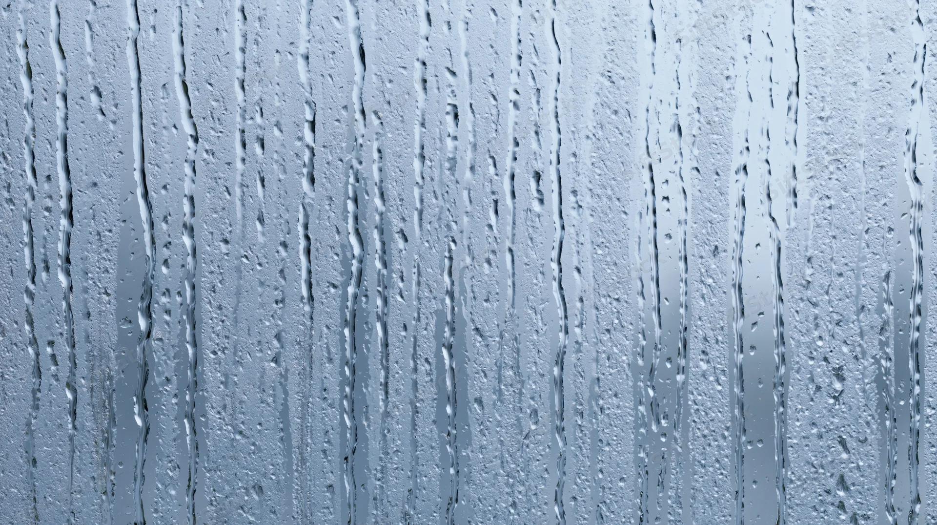 Raindrops streaking down a glass window surface in a close-up view
