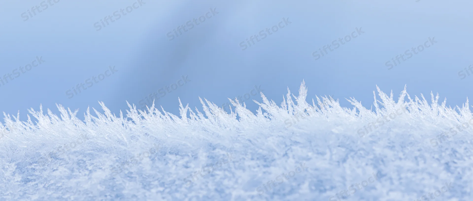 Close-up of frost crystals along the edge of a snow surface against a blue sky