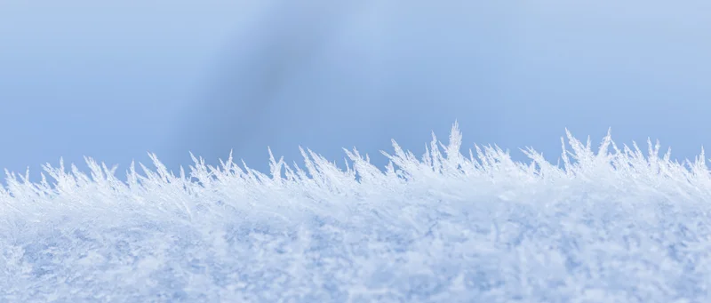 Close-up of frost crystals along the edge of a snow surface against a blue sky