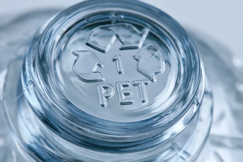 Close-up of the bottom of a clear plastic bottle showing embossed recycling symbol and PET label