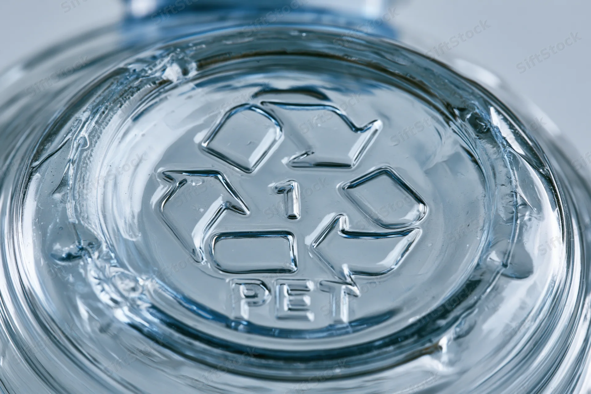 Close-up of embossed recycling symbol on bottom of clear plastic bottle