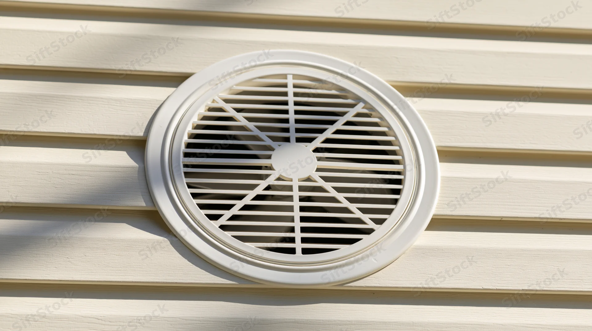 Circular ventilation grille mounted on cream-colored horizontal siding of a house exterior