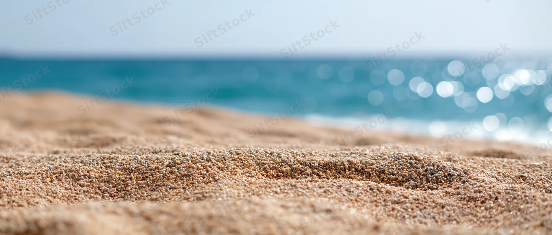 Close-up of dry sandy beach surface with ocean in the background