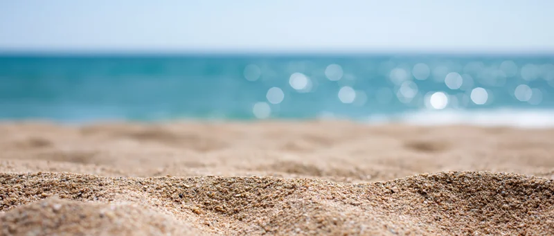 Close-up of dry sandy beach surface with blurred ocean in background