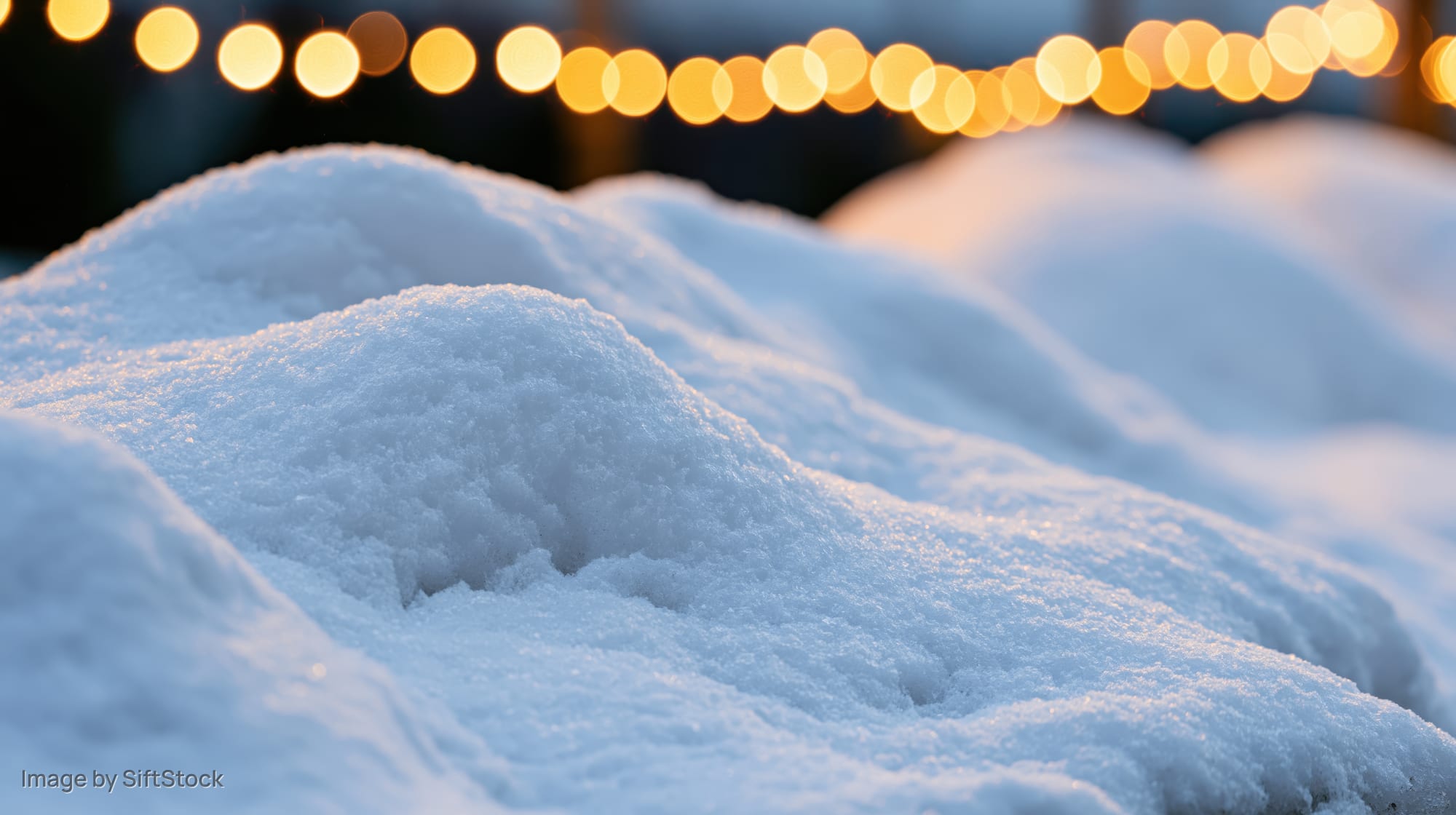 Closeup of soft snow mounds gently lit by warm string lights in the evening